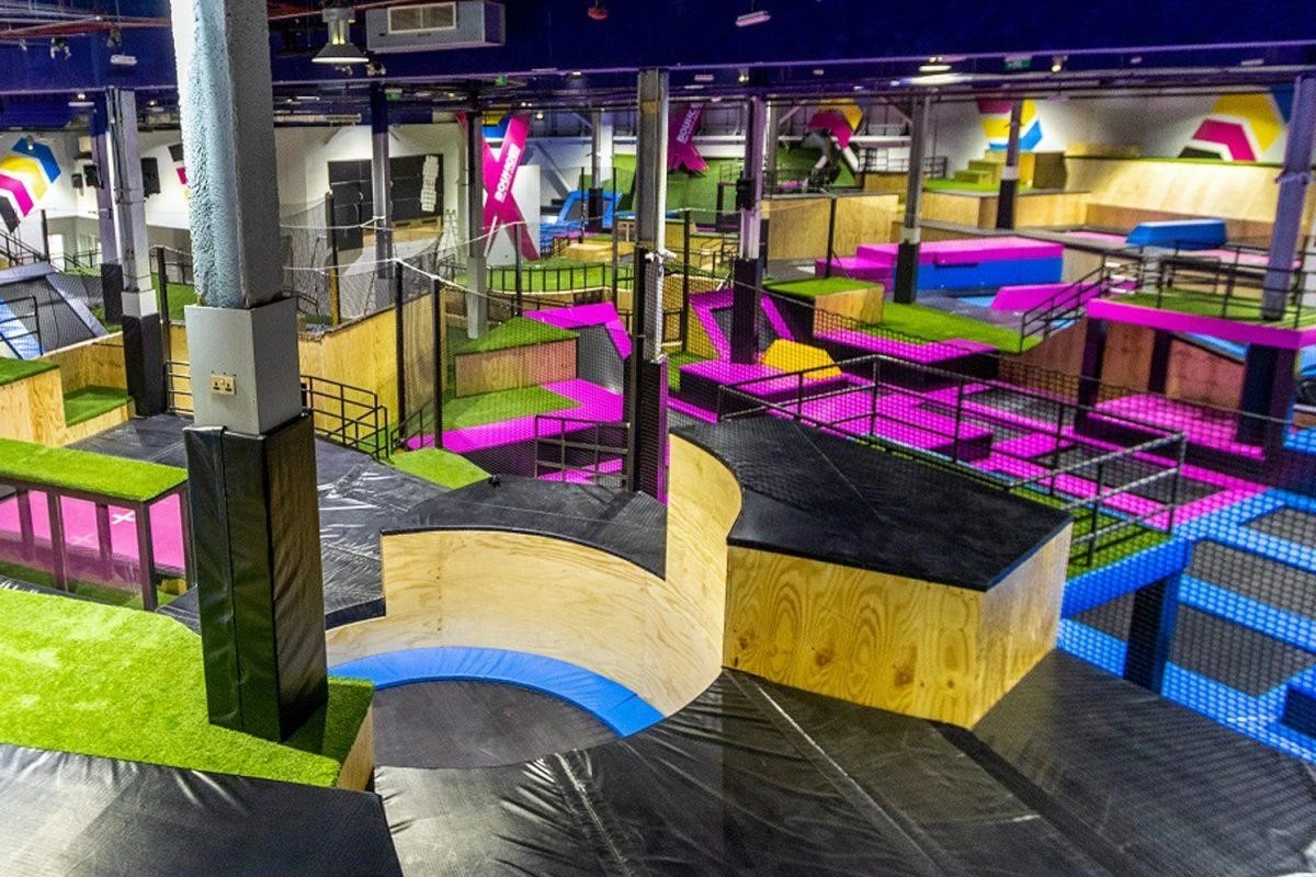 Large indoor trampoline park with colorful trampolines, angled ramps, and soft padded obstacles for jumping and freestyle activities