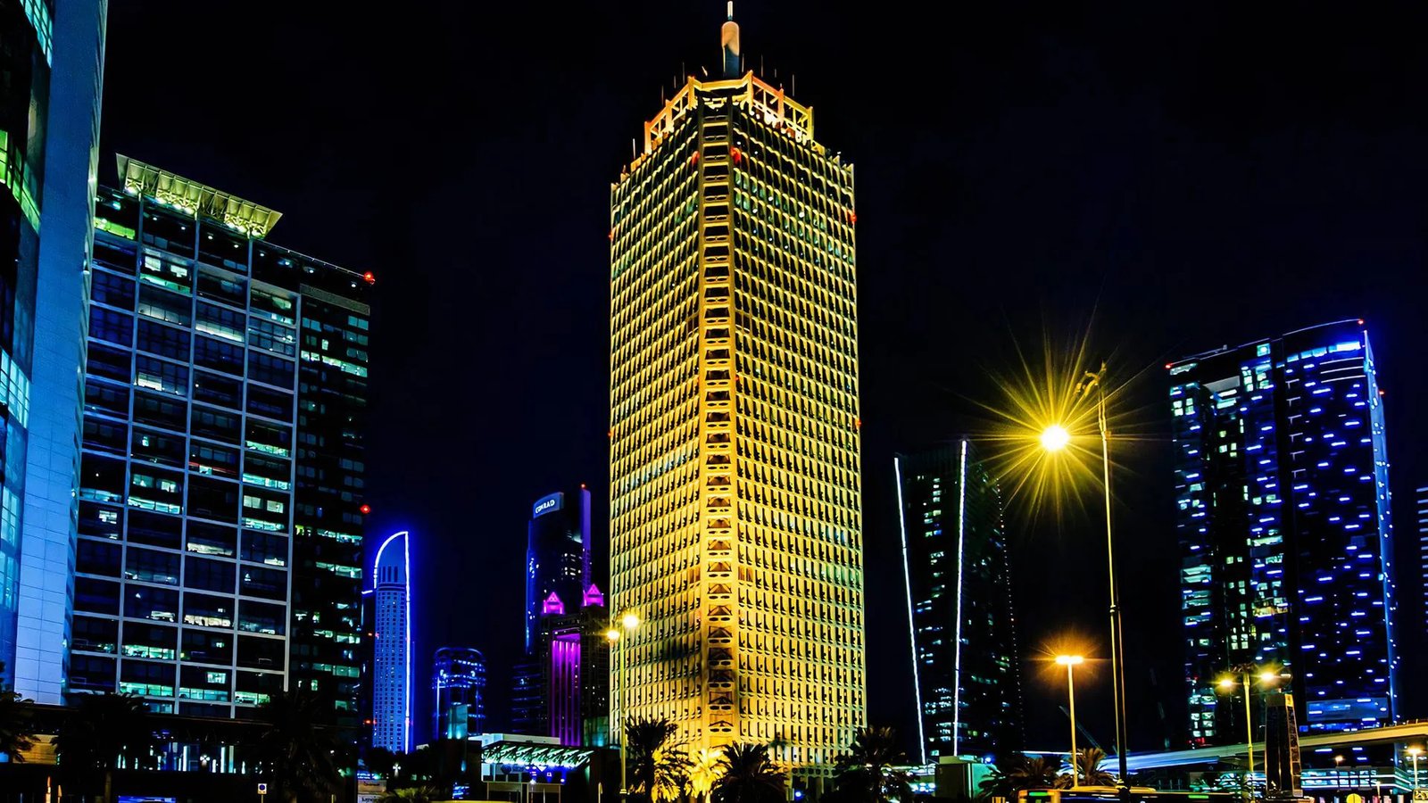 The iconic Dubai World Trade Center building stands out in golden light at night.