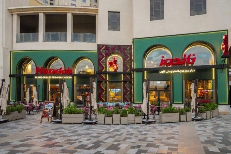 Interior view of Nando’s JBR Dubai with wooden tables, colorful wall art, hanging lights, and cozy dining setup