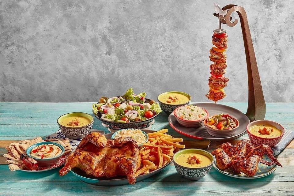 Grilled PERi-PERi chicken skewers served with spicy rice, corn on the cob, fries, and dipping sauces at Nando’s JBR Dubai
