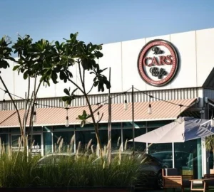Exterior view of The CARS Café at Dubai Autodrome with outdoor seating, greenery, and the café’s logo on the building