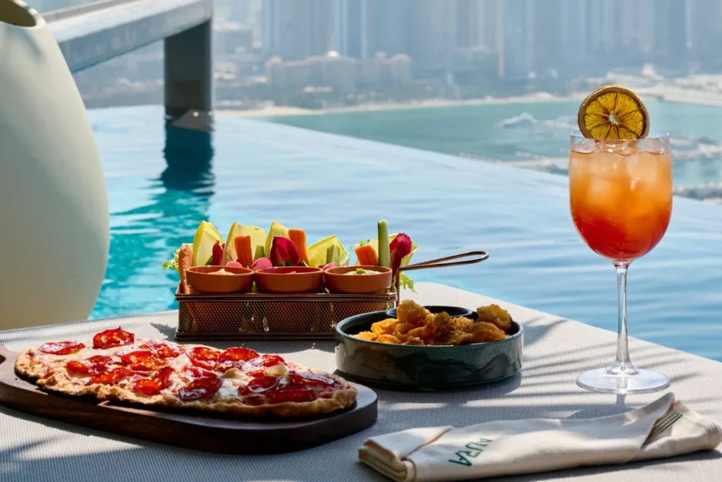 Infinity-edge pool with lounge chairs, lush greenery, and panoramic Dubai skyline views from AURA SkyPool