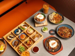 A rich spread of Asian fusion dishes from 77 Asia Restaurant, featuring noodles, rice bowls, bento boxes, iced tea, and more.