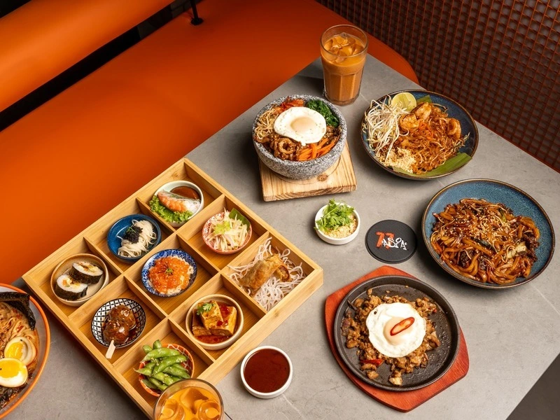 A rich spread of Asian fusion dishes from 77 Asia Restaurant, featuring noodles, rice bowls, bento boxes, iced tea, and more.