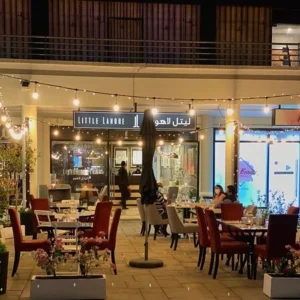 An image of the outside setting of a little Lahore food place in Dubai, showcasing wooden tables and soft cushioned chairs on a marble floor and small fairy lights.