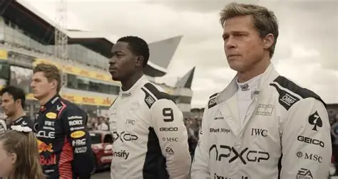 Brad Pitt and Damson Idris stand side by side on the Formula 1 starting grid, wearing APXGP racing suits.