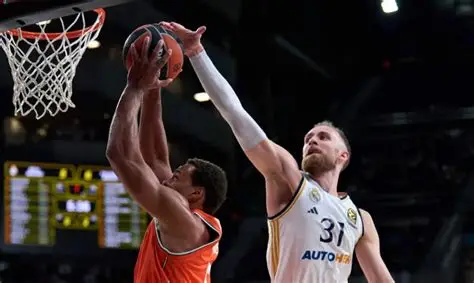 Dzanan Musa in a white jersey blocks a dunk attempt by an opponent in an orange jersey.