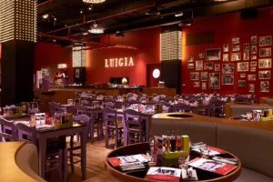 Interior view of Luigia Dubai at Rixos JBR with rows of wooden tables and red accent walls.