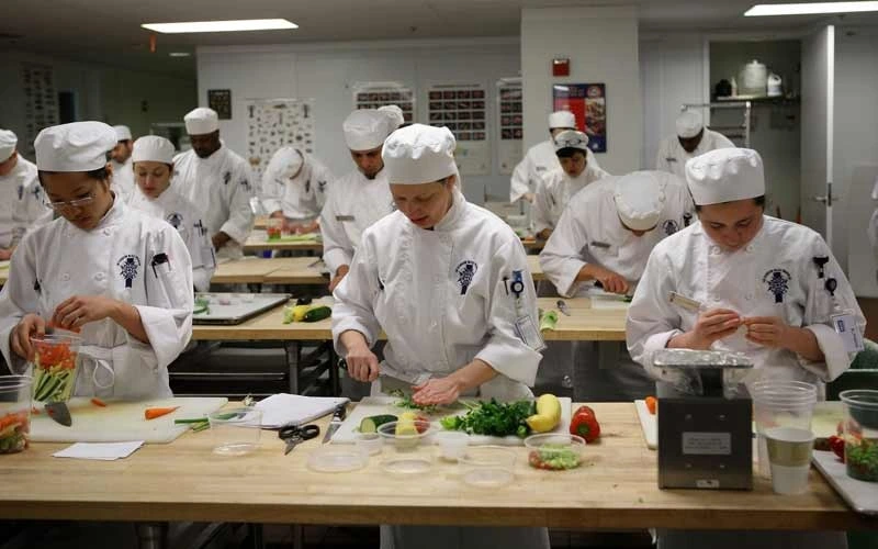 A chef instructing students in a professional cooking academy kitchen.