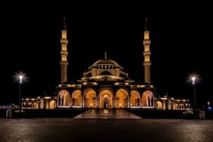 Night view of a beautifully designed Sharjah mosque with twin minarets and an arched entrance.