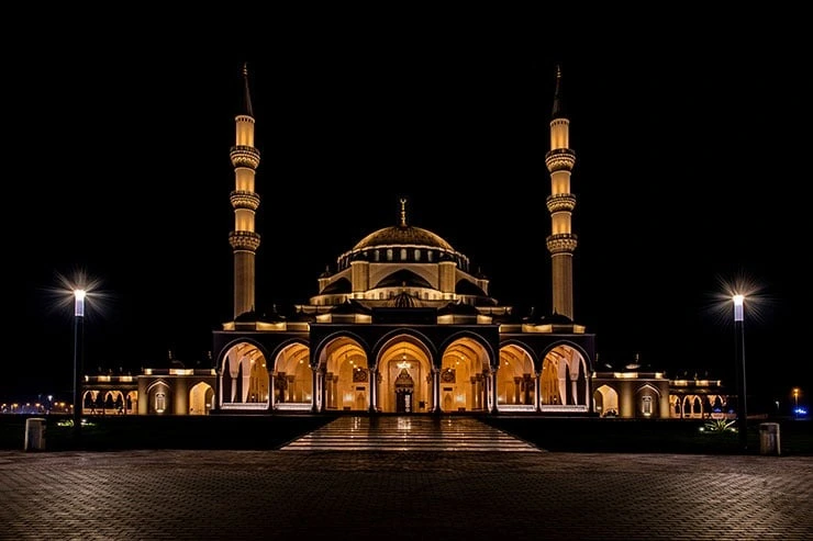 Night view of a beautifully designed Sharjah mosque with twin minarets and an arched entrance.