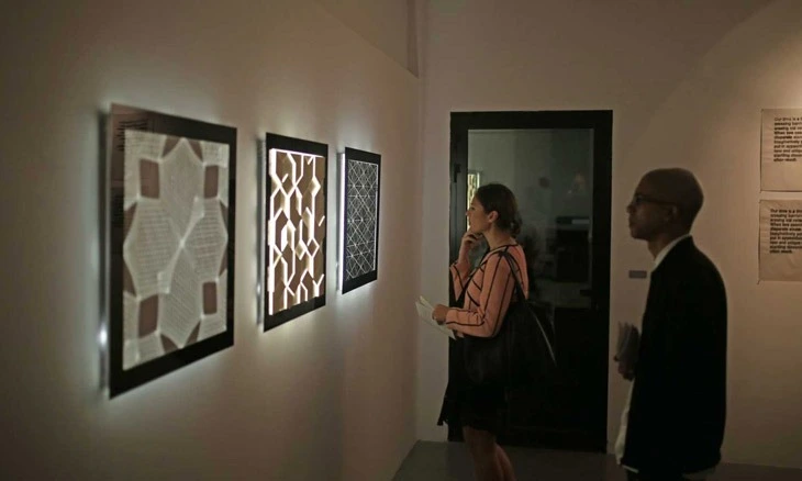 Two foreign visitors admire framed artworks hanging on the grey walls of Taksheel Gallery.