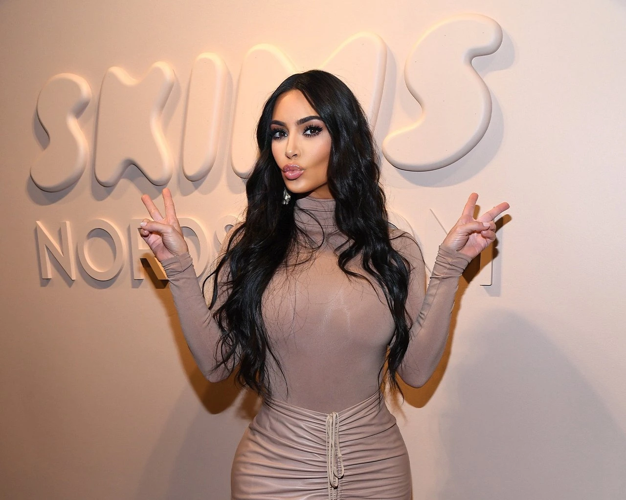 Kim Kardashian posing with peace signs in front of the SKIMS Nordstrom logo